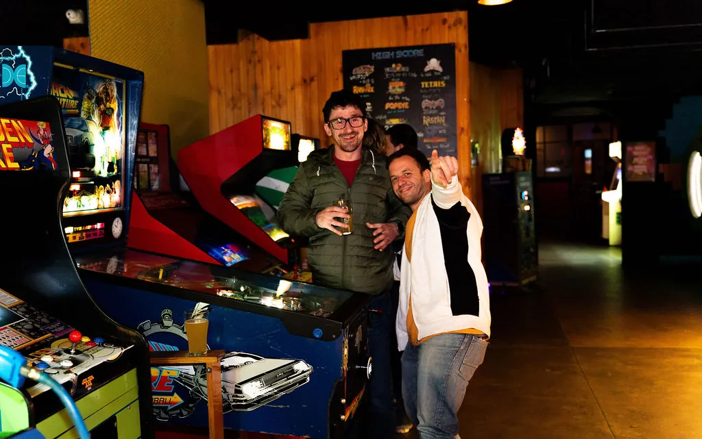 Two mates with drinks posing among the pinball machines at Bartronica