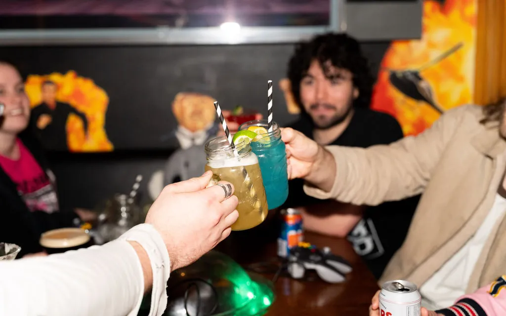 Friends clinking cocktails across a booth table at Bartronica