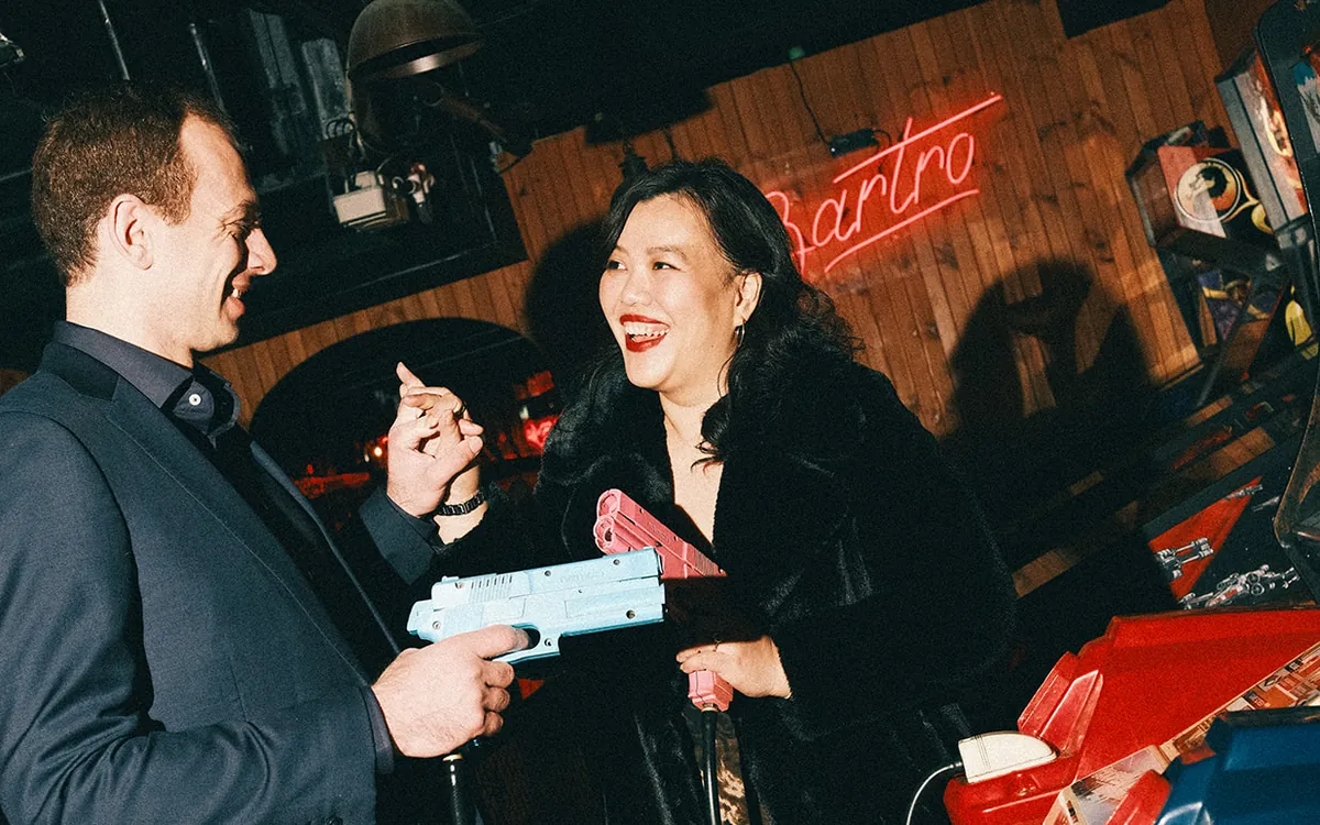 Couple laughing as they play a light gun arcade game under the Bartronica neon sign